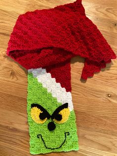 a crocheted scarf with an angry grin face on it sitting on top of a wooden floor