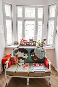 a couch with two faces painted on it in front of a window and wooden floor