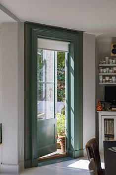 an open door leading to a dining room with potted plants in the window sill