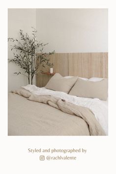 a bed with white sheets and pillows next to a plant