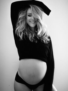 a pregnant woman wearing a hoodie and panties poses for a black and white photo