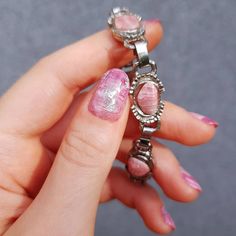 a woman's hand with pink and white nail polish holding a silver chain bracelet