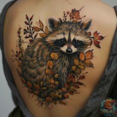 the back of a woman's shoulder with a raccoon and leaves tattoo on it