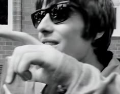 a woman wearing sunglasses brushing her teeth in front of a brick wall and holding a toothbrush