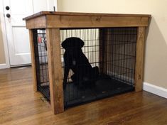 a black dog sitting in a cage on top of a hard wood floor next to a door