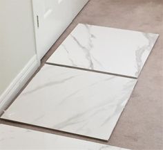 two white marble tiles laying on the floor next to each other in a room with beige carpet