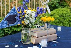 blue table cloth with yellow and white flowers in vases, books and graduation cap