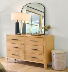 a dresser with a mirror, lamp and basket on the floor in front of it