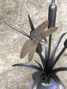 a dragonfly figurine sitting on top of a metal planter next to a wall