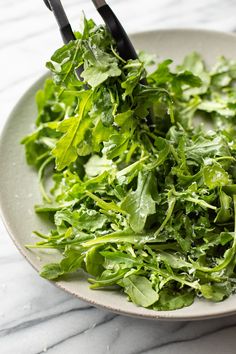 a white plate topped with green leafy vegetables on top of a marble countertop