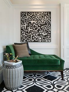 a green couch sitting on top of a black and white floor next to a painting