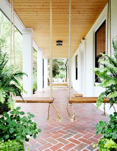 a porch swing with rope hanging from it's sides and plants on either side