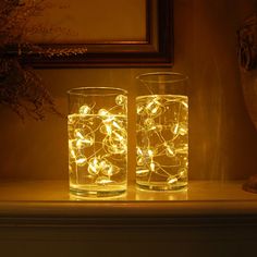 two glasses with lights in them sitting on a mantle