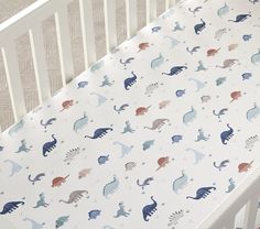 a crib sheet with dinosaurs on it and the words pottery barn kids written in red