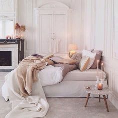 a bed with blankets, pillows and candles on top of it in a room that has white walls