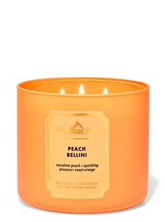 an orange candle is sitting on a white surface with the words peach bellini written in gold