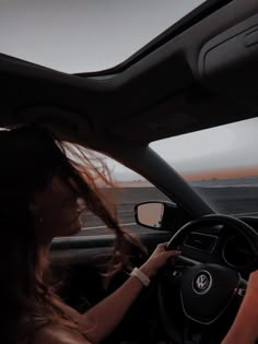 a woman driving a car on the road at dusk with her hair blowing in the wind