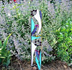 a blue and white sculpture sitting in front of some purple flowers with lots of beads on it