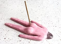 a pink hand with a stick sticking out of it's palm on a white surface