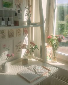 a white desk topped with lots of flowers next to a window filled with books and vases