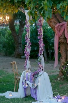 an outdoor wedding setup with purple flowers hanging from the trees and candles on the ground