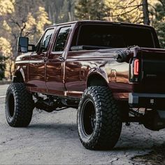 a large red truck parked on top of a dirt road next to trees and bushes