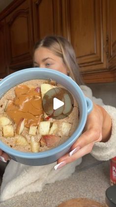 a woman is holding a bowl of oatmeal with apples and peanut butter