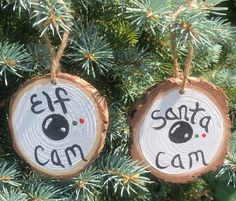 two wood slices with the words santa and cam on them hanging from a pine tree