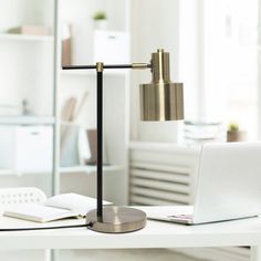 a desk lamp sitting on top of a white table next to a laptop and book