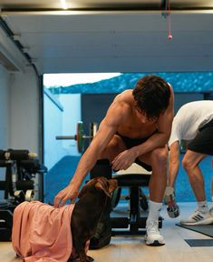 a man is doing exercises with his dog in the gym while another watches from the bench