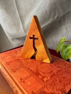 an orange book with a wooden cross on it and a potted plant in the background