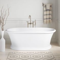 a white bathtub sitting on top of a wooden floor next to a vase with flowers