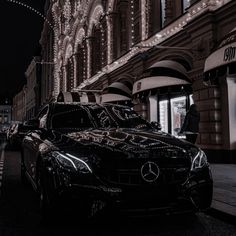 a black car parked on the side of a street next to a tall building at night