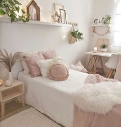 a white bed with pink pillows and blankets on it in a room filled with furniture