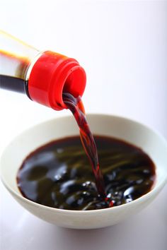 the sauce is being poured into a white bowl with black liquid in it and a red bottle on top