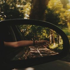 a person's hand is seen in the rear view mirror of a car as it drives down a road