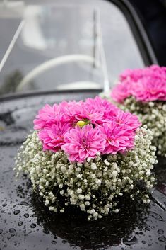 pink and white flowers sitting on the hood of a black car with raindrops