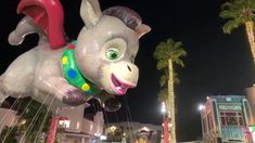 an inflatable animal balloon floats through the air with palm trees and buildings behind it