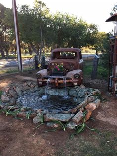 an old truck is parked next to a small pond with flowers in the back ground