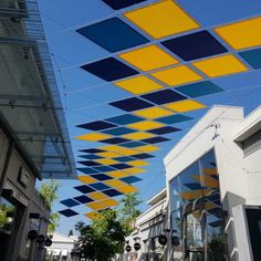 the blue and yellow squares are suspended from the ceiling in this city street lined with buildings