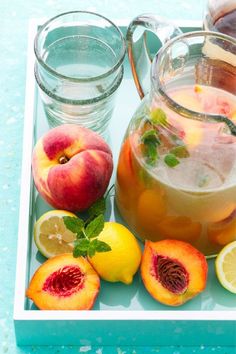 peaches, lemons and water are on a tray next to pitchers of tea