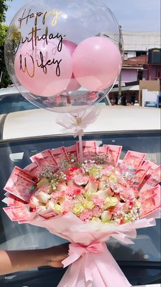 a bouquet of flowers and balloons sitting on the hood of a car with happy birthday wishes written on it