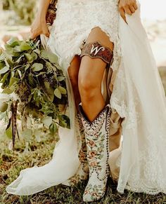 a woman in cowboy boots is sitting on the ground with her legs crossed and holding flowers