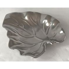 a metal leaf shaped dish sitting on top of a white tablecloth covered floor next to a wall