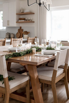 a dining room table set for christmas with candles and greenery on the table top