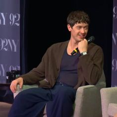 a man sitting in a chair talking into a microphone