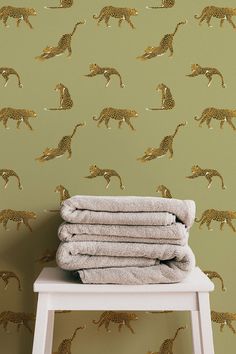 towels stacked on top of a stool in front of a wall with gold leopards