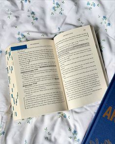 an open book sitting on top of a bed next to a blue book bag and white sheets