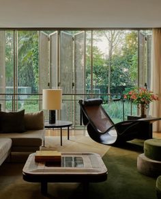 a living room filled with furniture next to tall glass windows covered in plants and trees