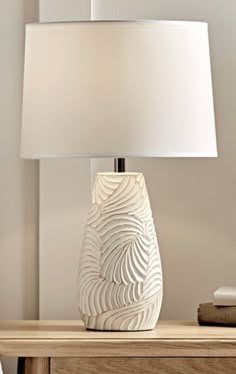 a white lamp sitting on top of a wooden table next to a night stand with a book